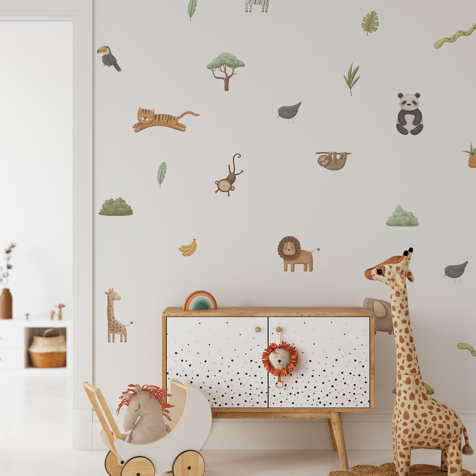 The childrens room features My Stores Safari & Jungle Animal Stickers with tigers, monkeys, pandas, and giraffes. A large plush giraffe stands by a toy cart holding a plush lion, creating an adventurous and playful nursery decor.