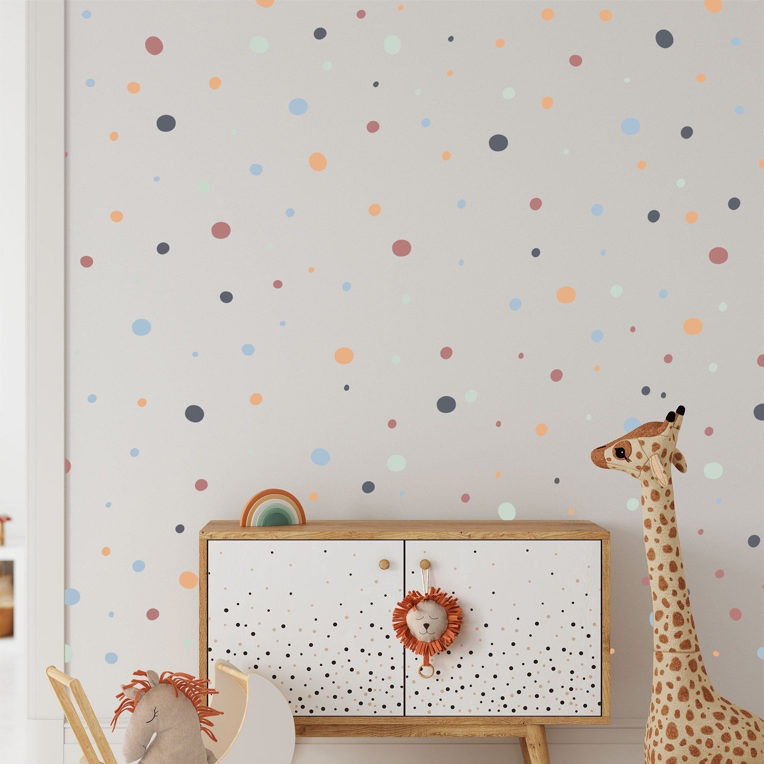 A childrens room features a white cabinet with a lion face handle, accompanied by a plush giraffe toy. The wall is decorated with My Stores Boho Polka Dots Stickers in orange, blue, and green. A stuffed horse toy peeks out, enhancing the playful decor.