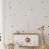 A childrens room features a white cabinet with a lion face handle, accompanied by a plush giraffe toy. The wall is decorated with My Stores Boho Polka Dots Stickers in orange, blue, and green. A stuffed horse toy peeks out, enhancing the playful decor.