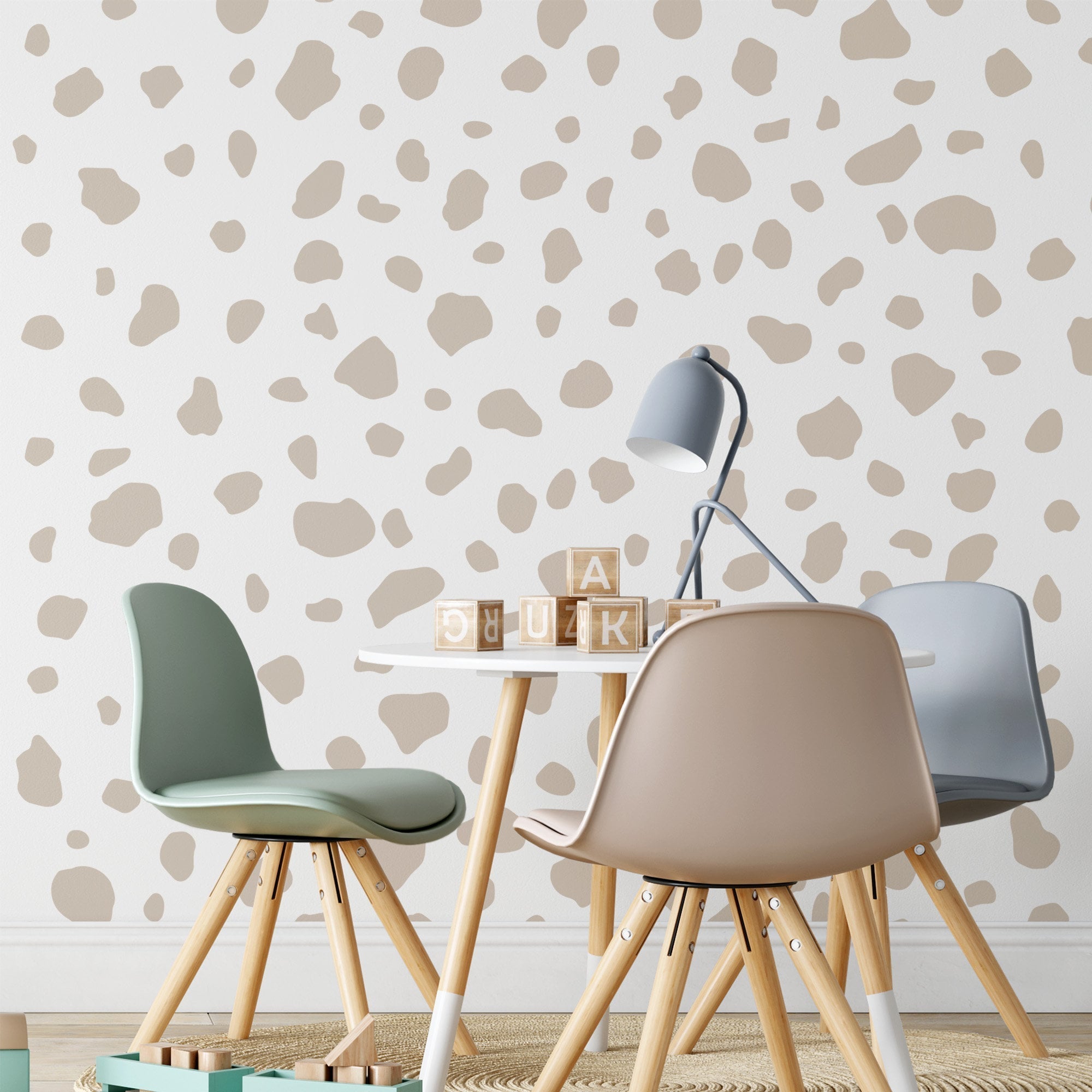 A small modern table with pastel chairs complements a room adorned by My Stores Dalmatian Spot Stickers on the beige and white wall. Wooden blocks and a lamp sit on the table, while a woven rug brings warmth to the floor.