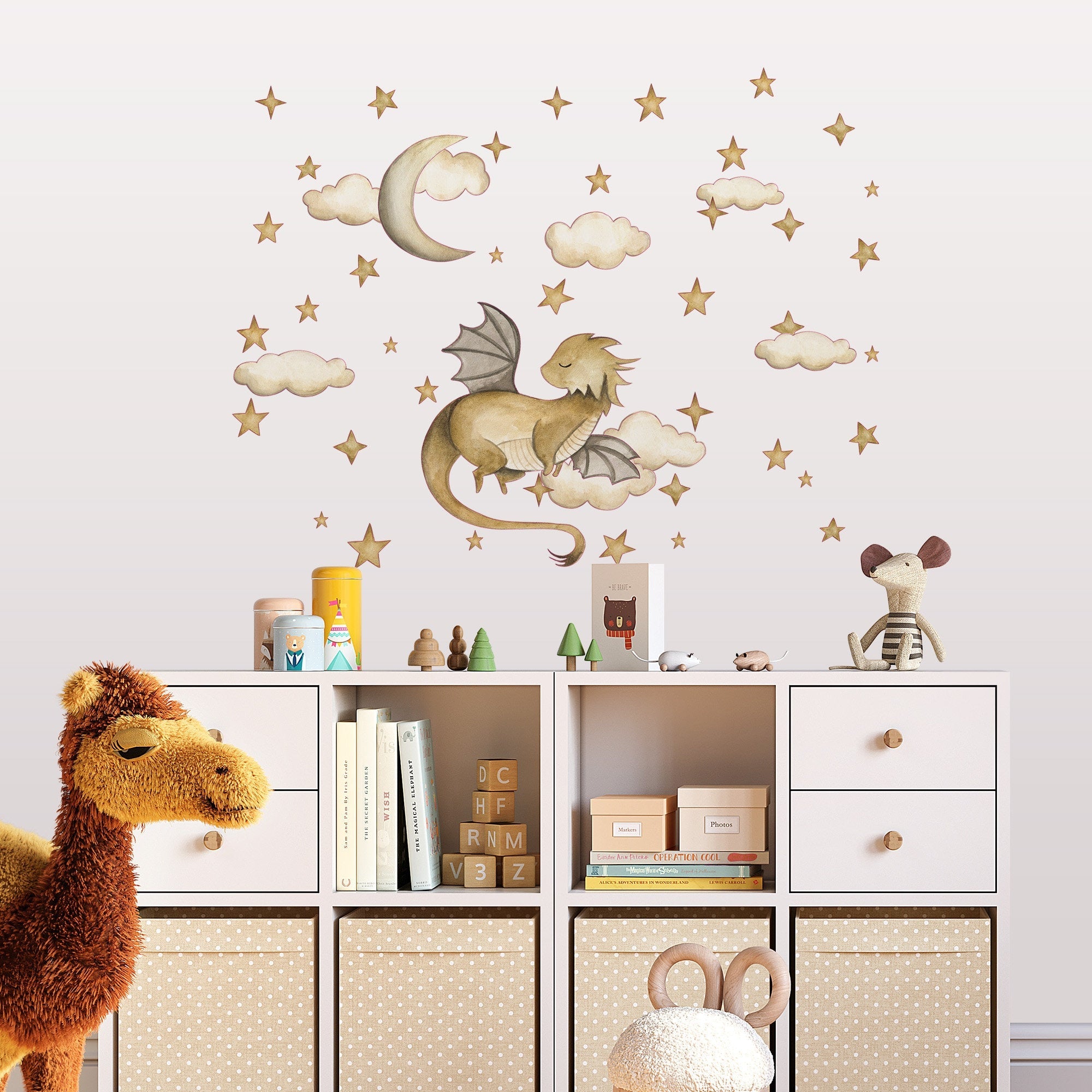 A cozy childrens room showcases My Stores Golden Dragon Stickers, featuring a whimsical sleeping dragon among clouds, stars, and a crescent moon. A stuffed camel sits in the foreground, while shelves beneath the removable wall decals are filled with toys and books.