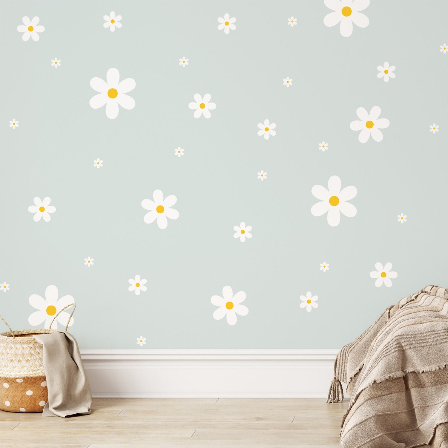 A cozy room with light green walls features My Stores Daisy Wall Decals for a whimsical touch. A woven basket and beige blanket on the light wooden floor complete the nursery decor with warmth and charm.