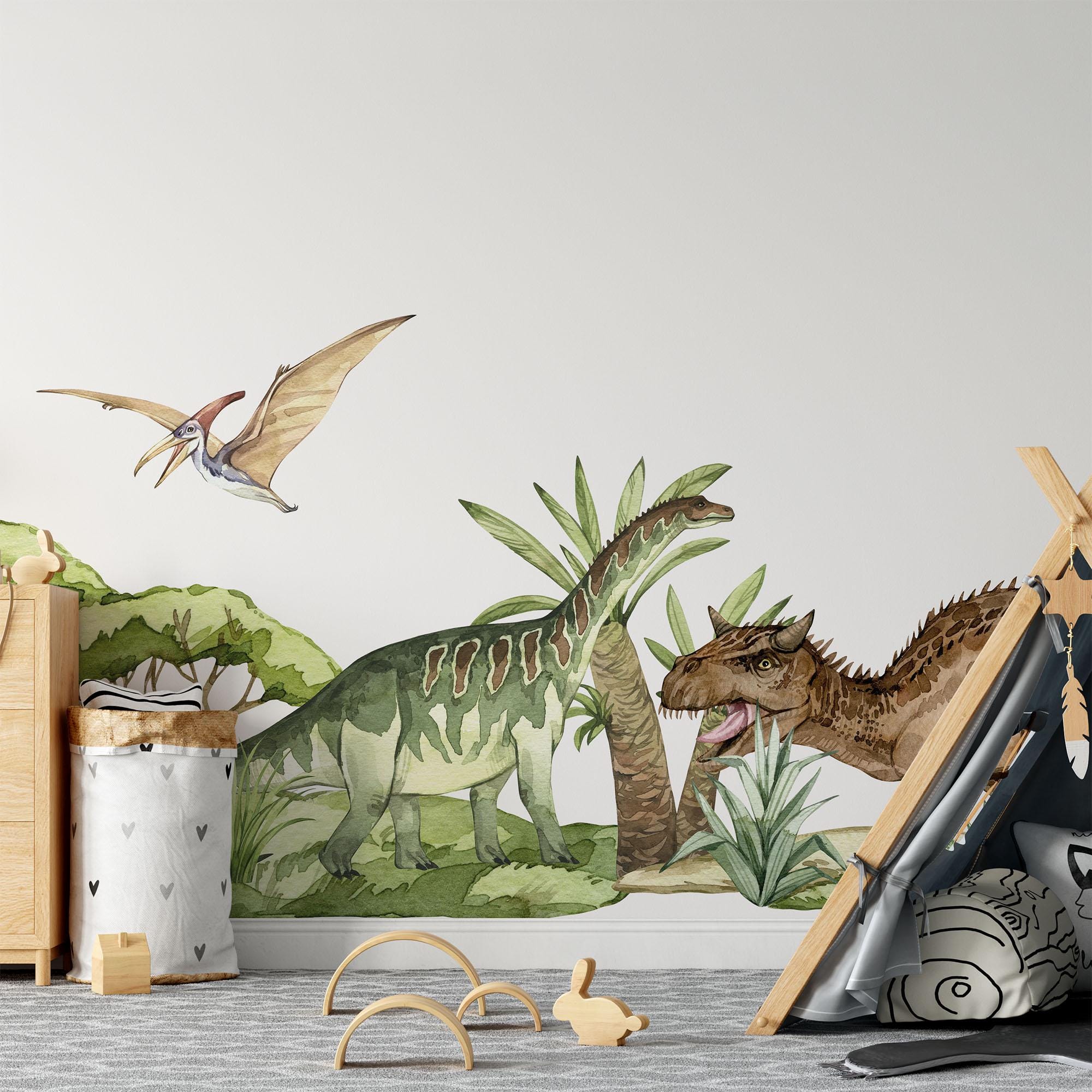 My Stores Dinosaur Nursery Stickers turn a childrens room into an adventure with a dinosaur-themed mural featuring a pterodactyl and two dinosaurs among plants. The nursery is completed with a wooden dresser, laundry basket, teepee tent, and scattered toys.
