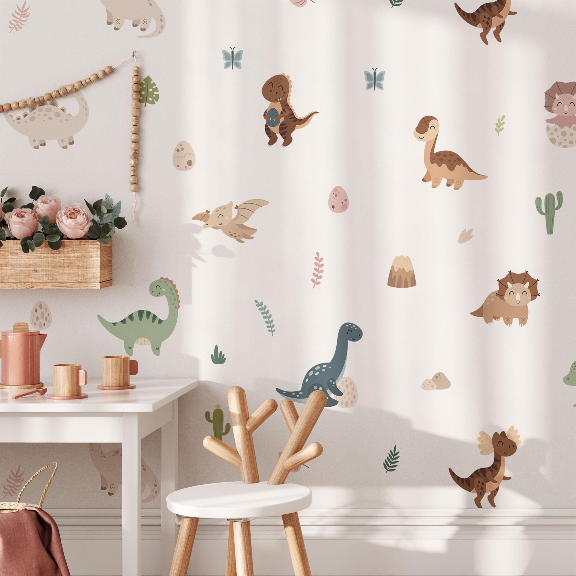 A childrens room features Fun Dinosaurs Stickers from My Store with colorful cartoon dinosaurs, eggs, and plants. A white desk holds pink flowers and containers, accompanied by a wooden chair with a branch-like backrest.