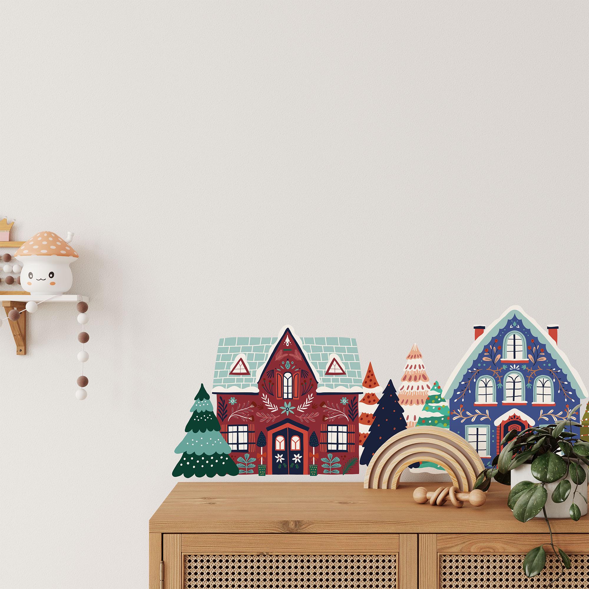 A wooden cabinet adorned with colorful miniature houses and trees stands against a light-colored wall. My Stores Festive Houses Wall Stickers add charm, while a shelf on the left holds a small decorative item. A rainbow-shaped wooden toy completes this delightful display.