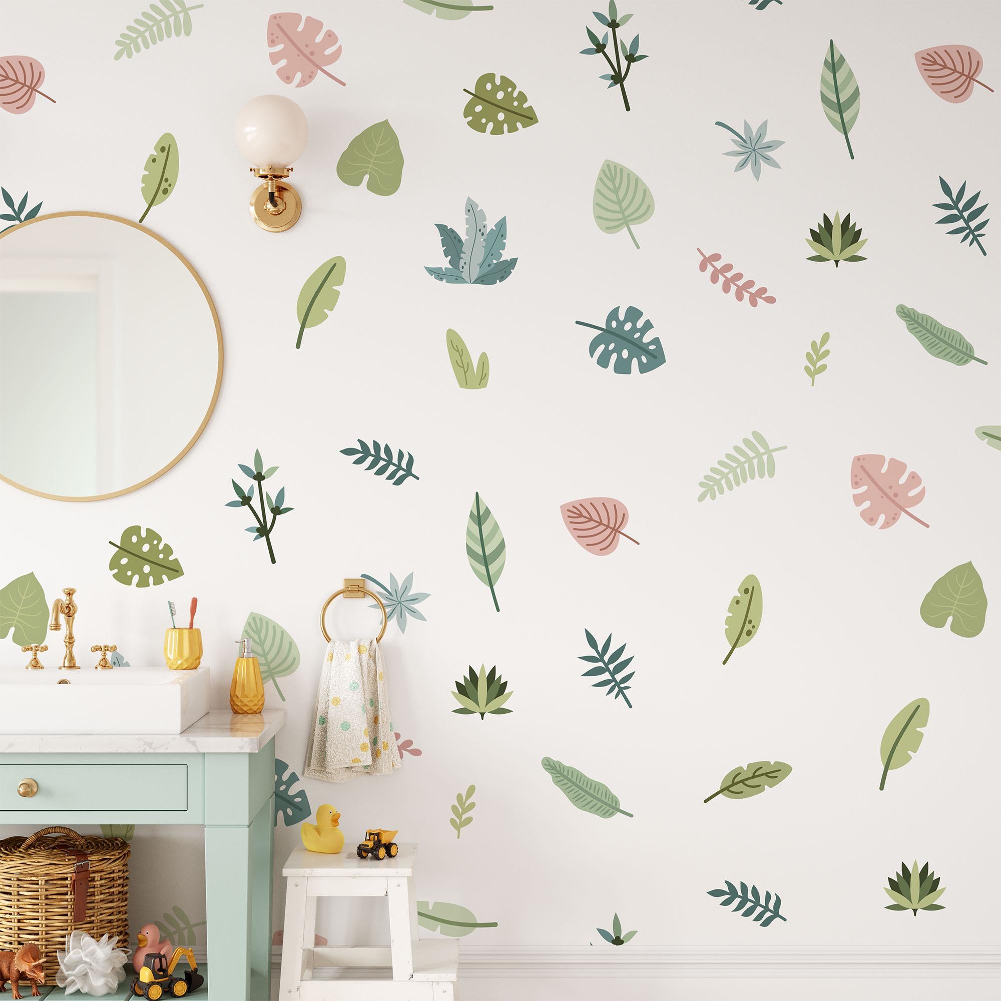 A bathroom features My Stores Tropical Leaves Nursery Wall Stickers, a light green vanity with two orange toothbrush holders, a duck figurine, and a round mirror. A towel hangs nearby and a small sconce is above the mirror.