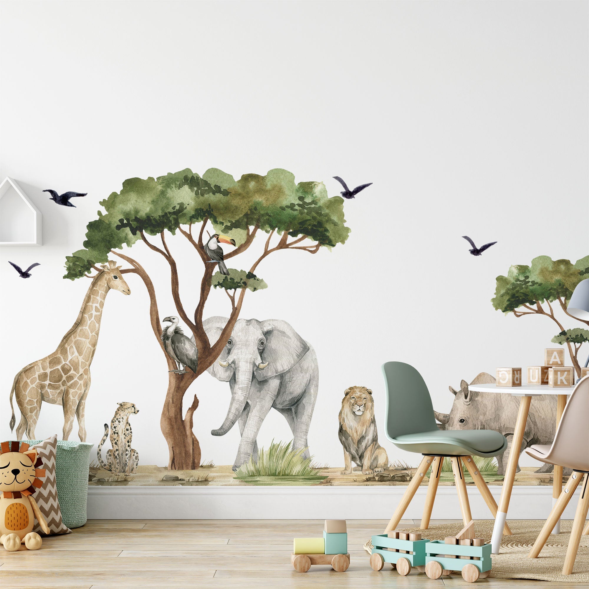 A childrens room showcases My Stores Safari Animals Nursery Stickers, featuring a giraffe, elephant, lion, cheetah, rhino, and birds near a tree. The space includes toys, a small table with colorful chairs, and a soft carpet.