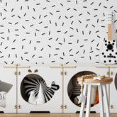 A childs room showcases My Stores Black Sprinkle Stickers on a white wall. A guitar is mounted on the wall, and wooden storage cubes store a zebra toy, teddy bear, and beads—ideal nursery decor that balances playful charm with functional storage.