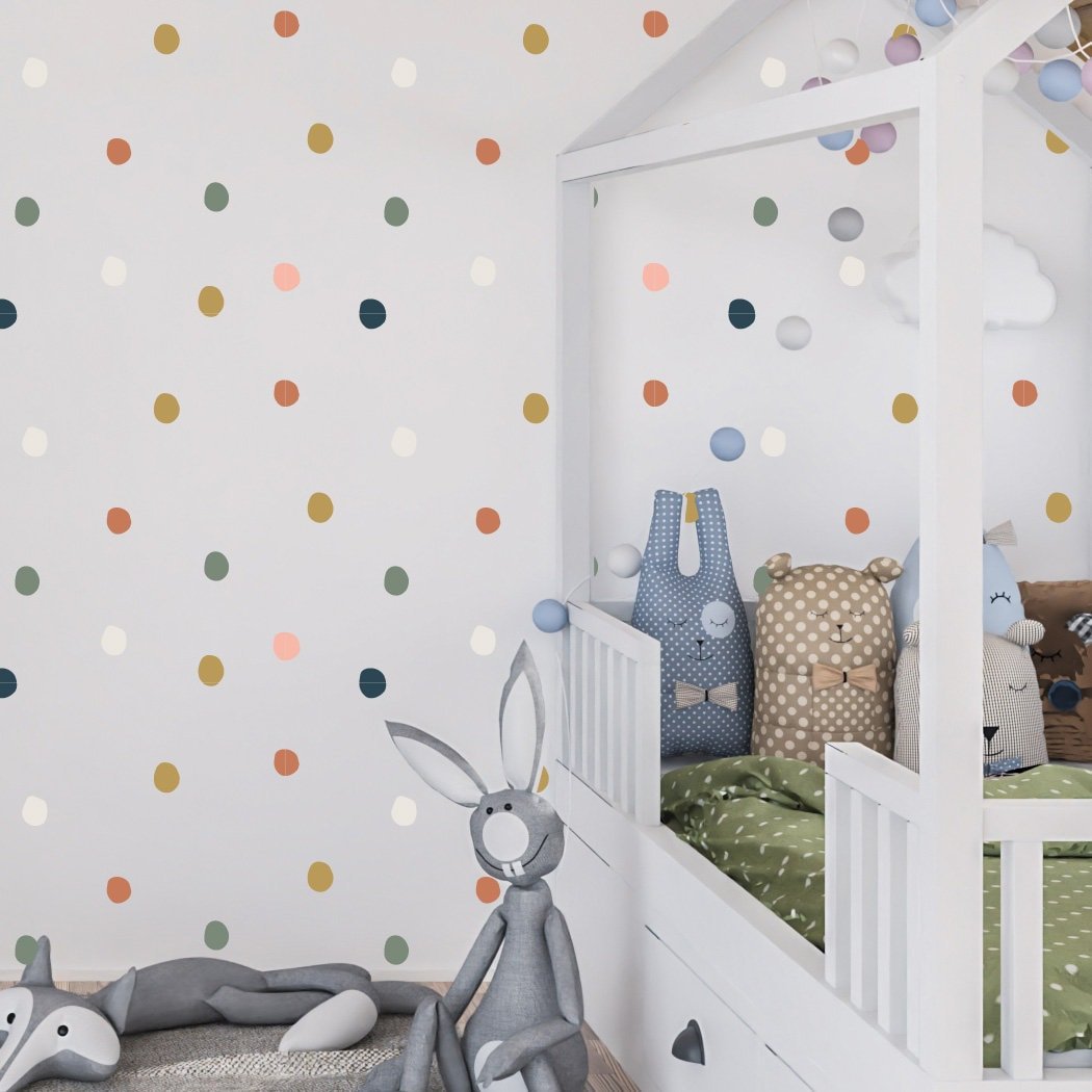 A childrens room with a white house-shaped bed and plush toys, including a gray rabbit. The wall features My Stores Coloured Dot Stickers, adding playful charm. Various pillows complete the cozy atmosphere, enhanced by the easily removable stickers.