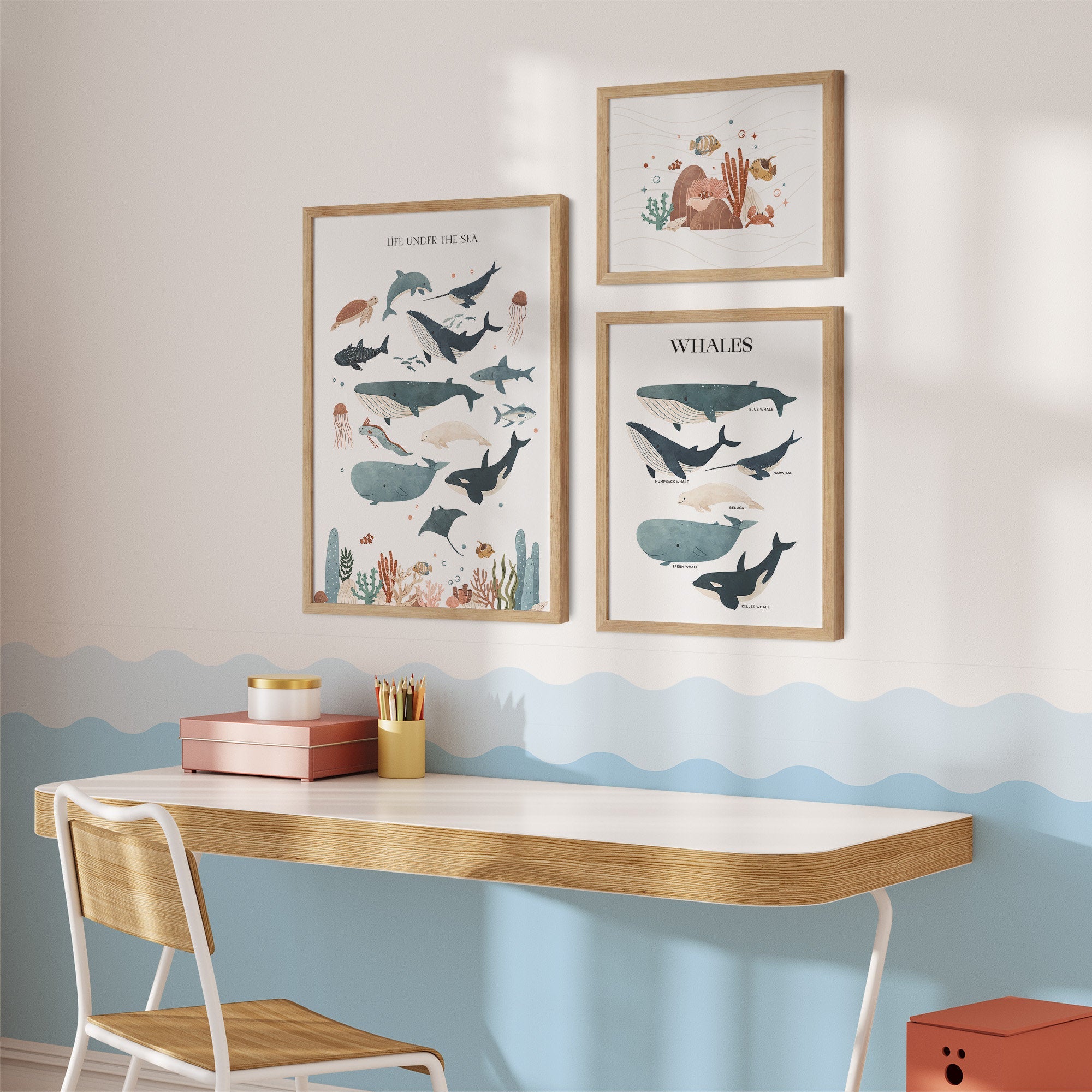 A bright nursery features a soft wood desk and chair. Above, three Sea Animals Nursery Prints by My Store display marine life themes like whales and fish alongside a decorative wave wall pattern, while the desk holds neatly arranged books and pencils.